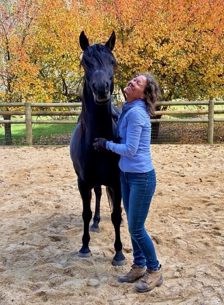 Woman in a yard standing and hugging a horse