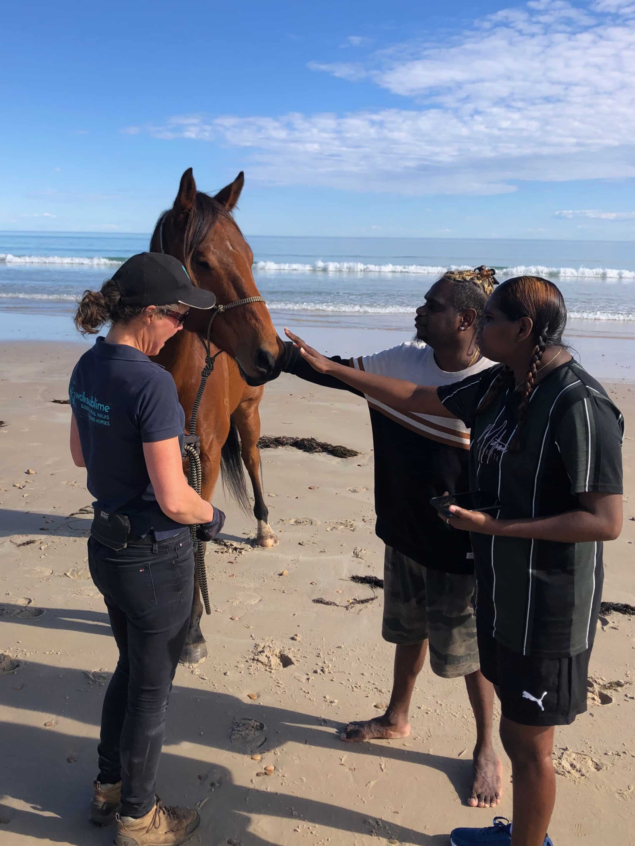 First Nations man and woman patting a horse on the beach