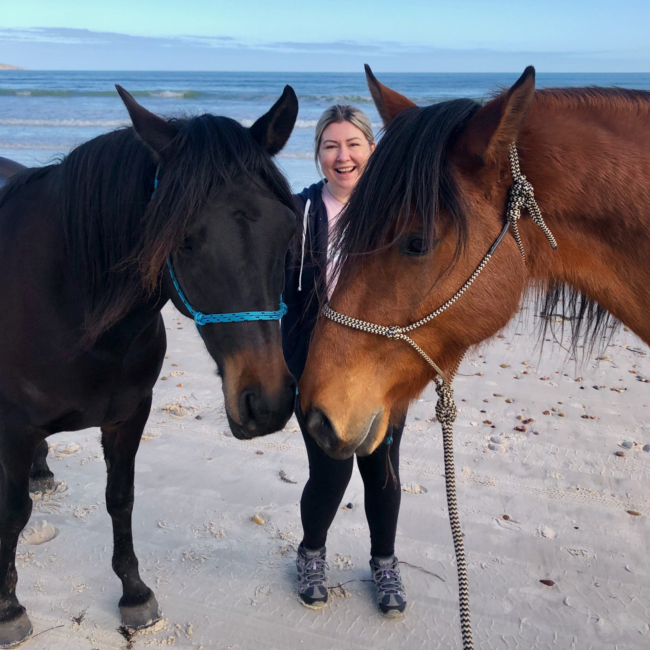 Lady standing with two horses at the beach